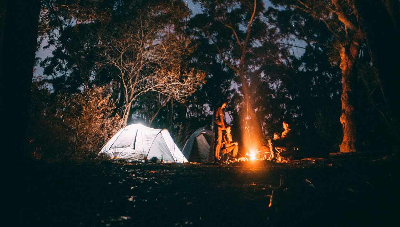it's night in the woods and there's a tent and a campfire with people around it