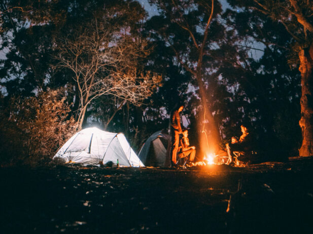it's night in the woods and there's a tent and a campfire with people around it