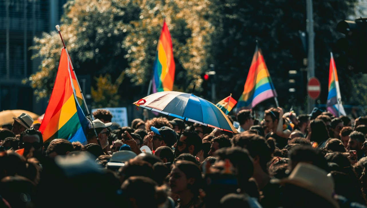 A crowd at a Pride Parade with rainbow flags in the background