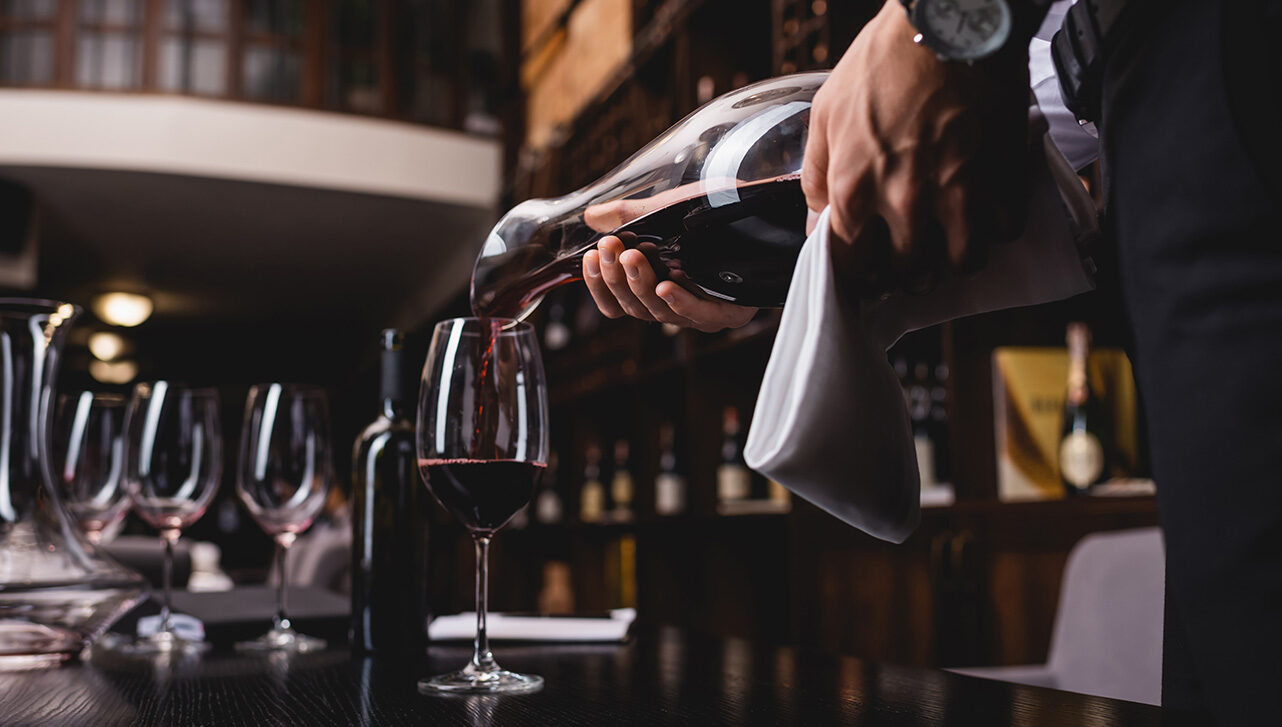 Selective focus of sommelier holding towel and pouring wine in glass on table in restaurant