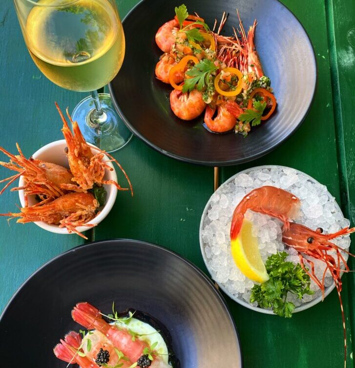 table display of various dishes with prawns and a glass of white wine