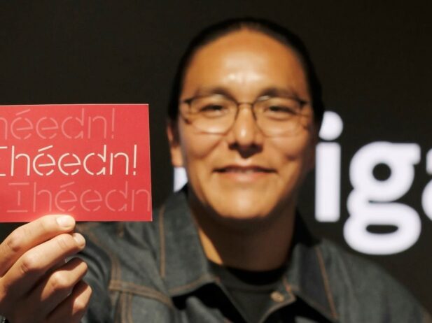 Leo Vicenti holding a red postcard printed with a custom type design that reads "Ihéédn!"