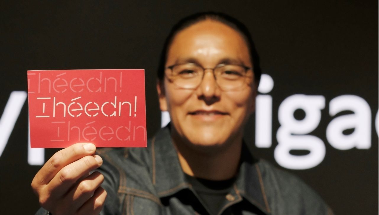 Leo Vicenti holding a red postcard printed with a custom type design that reads "Ihéédn!"